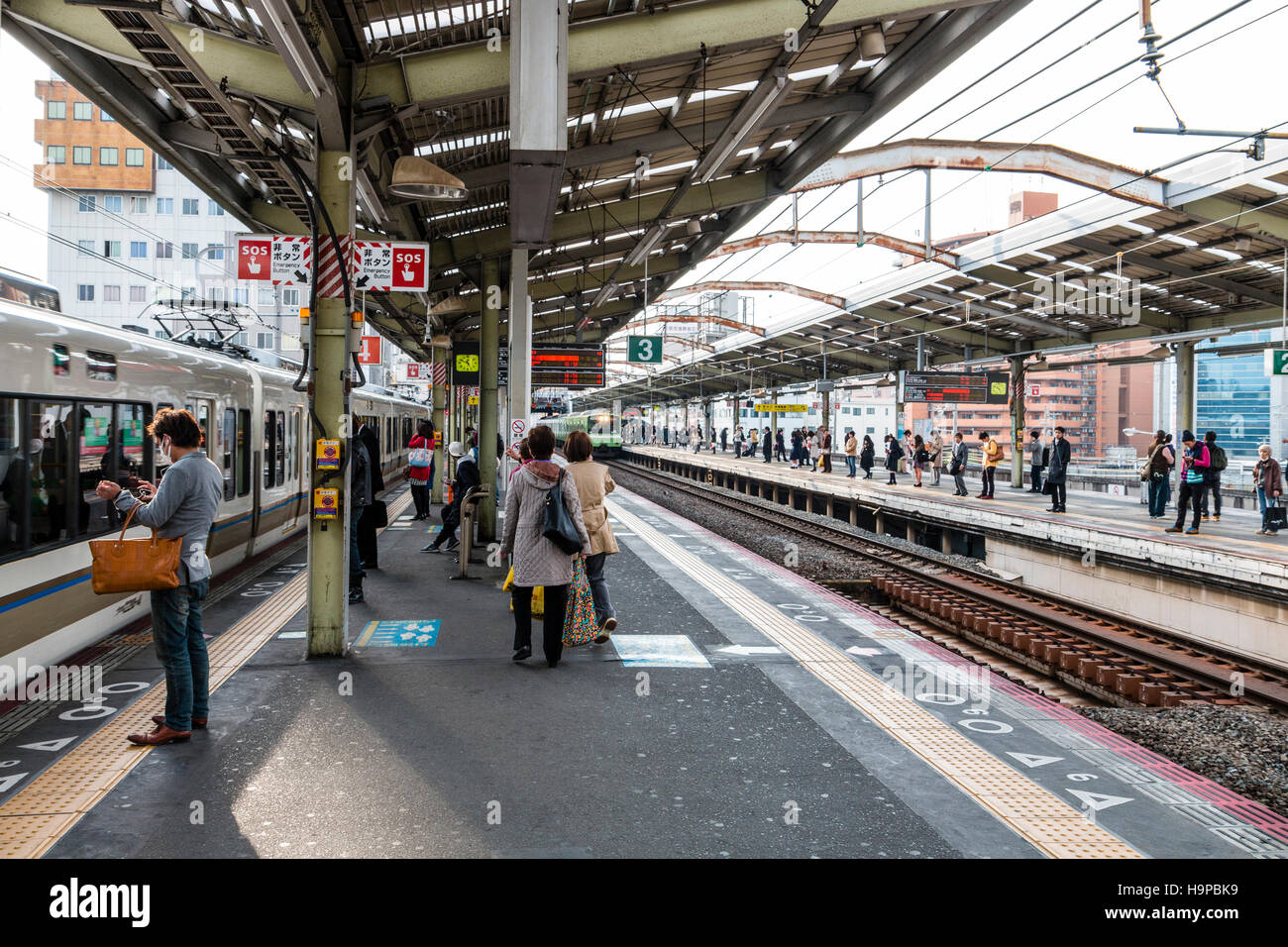 Giappone, JR SHIN-imamiya stazione sull'Osaka linea loop. Vista lungo la piattaforma, treni pendolari a piattaforma, persone in piedi in attesa. Foto Stock