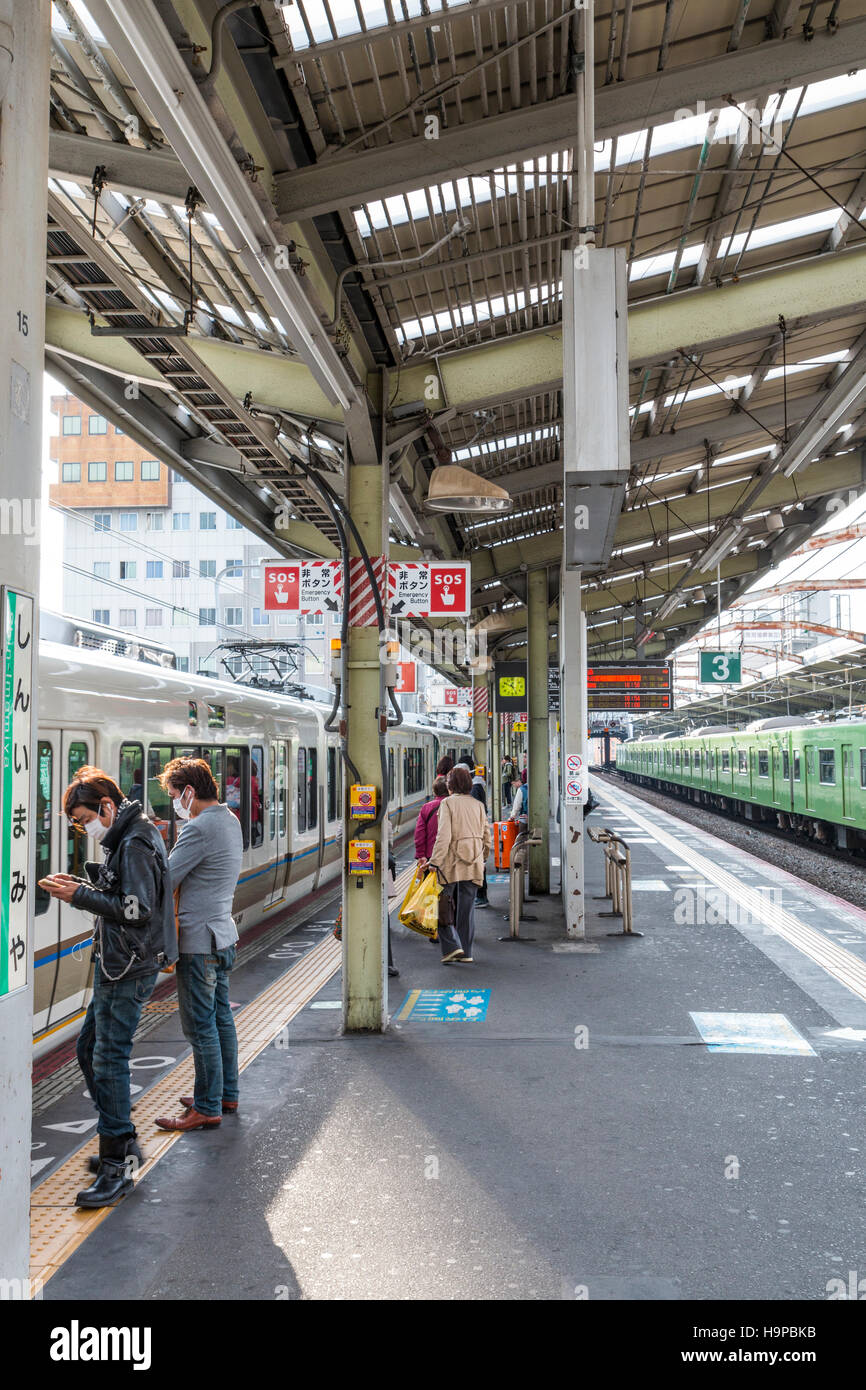 Giappone, JR SHIN-imamiya stazione sull'Osaka linea loop. Vista lungo la piattaforma, treni pendolari a piattaforma, persone in piedi in attesa. Foto Stock