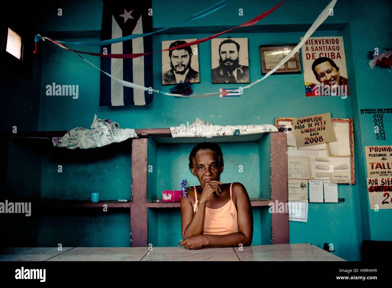 L'Avana, Cuba. 28 Luglio 2009 -- una donna cubana sta dietro il bancone, tenendo un fiore, di fronte ad una parete ricoperta da foto del rivoluzionario leader, Santiago de Cuba, Cuba. -- Il popolo di Cuba sono orgogliosi dei loro eroi. Esse hanno messo la foto del rivoluzionario cubano (leader Fidel Castro Che Guevara, Raul Castro) in abitazioni e luoghi di lavoro o nei negozi. | Verwendung weltweit/picture alliance Foto Stock