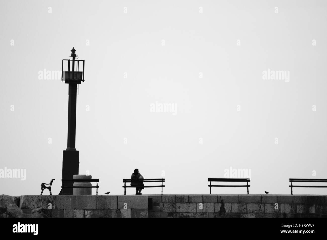 Da sola donna seduta su un banco di lavoro sul dock con il faro Foto Stock