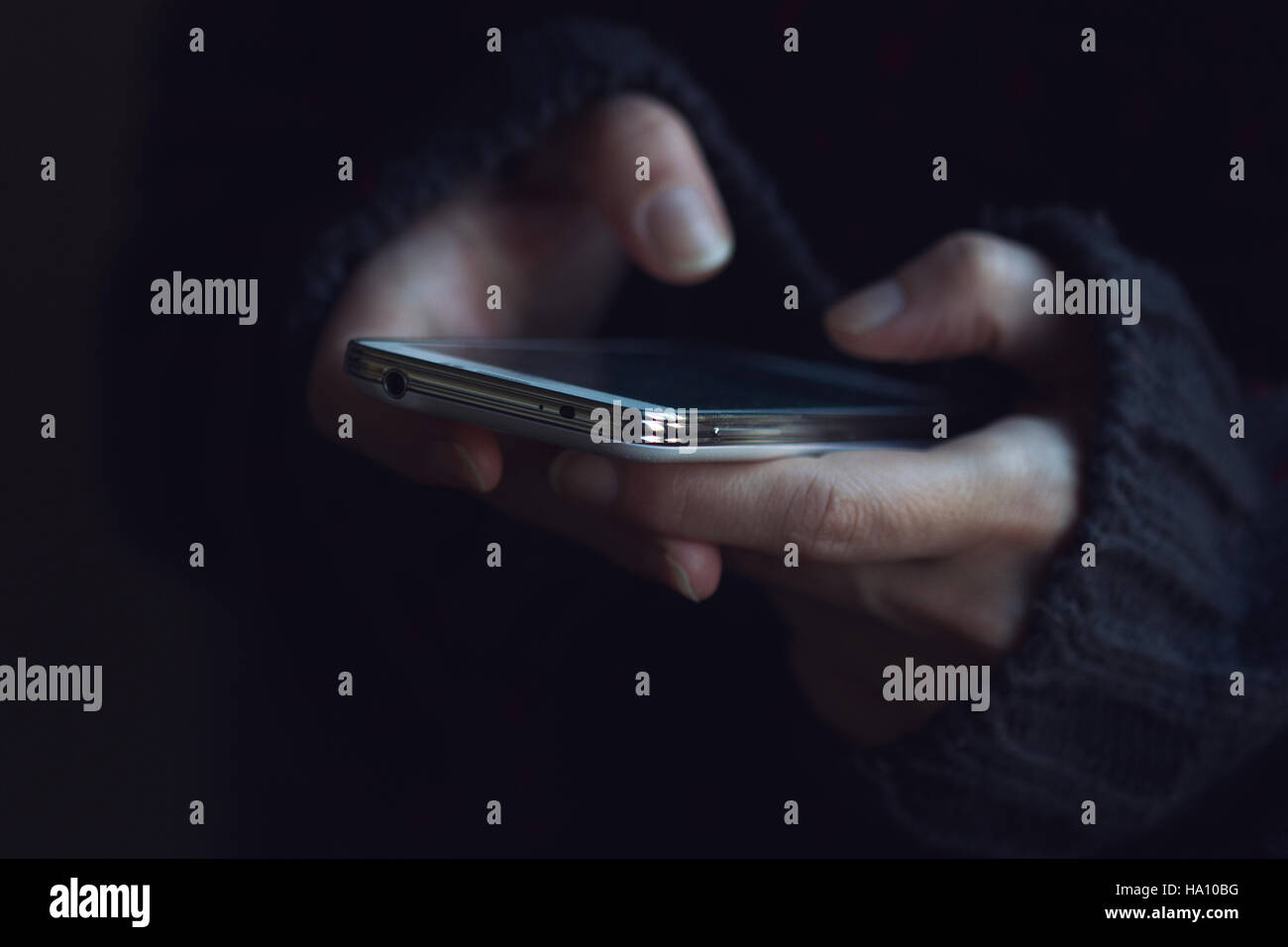 Vista frontale ravvicinata di una donna in maglione scuro mani tenendo un telefono e digitando Foto Stock