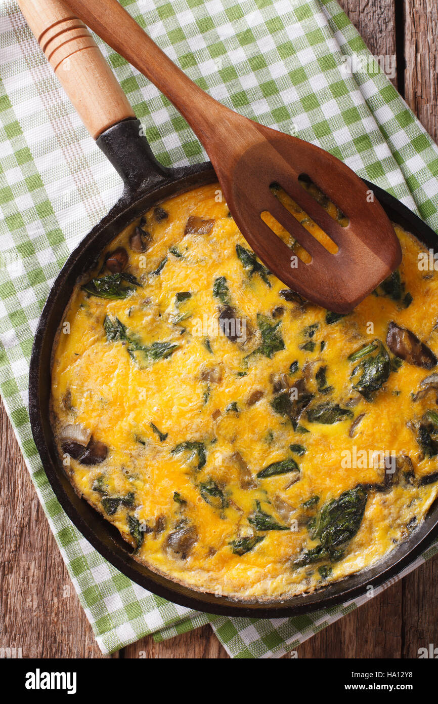 Deliziose omelette con spinaci, formaggio cheddar e i funghi in una padella vicino sul tavolo. Vista verticale da sopra Foto Stock
