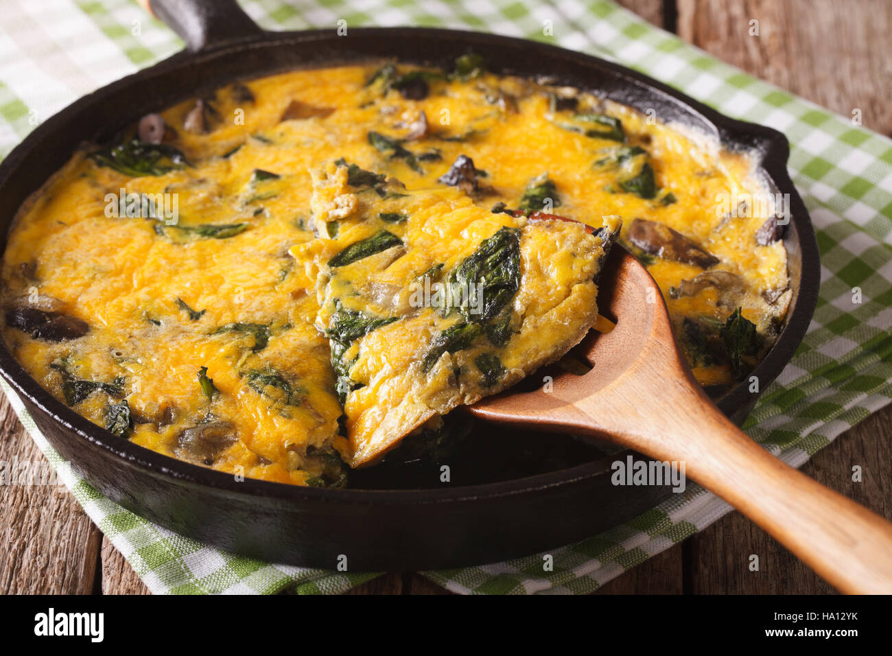 Deliziose omelette con spinaci, formaggio cheddar e i funghi in una padella vicino sul tavolo orizzontale. Foto Stock