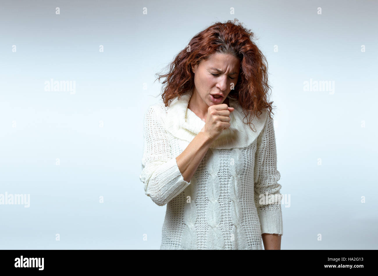 Attraente giovane donna in elegante moda inverno tosse permanente di elevare il suo pugno per la sua bocca in un concetto di assistenza sanitaria su bianco con spazio di copia Foto Stock