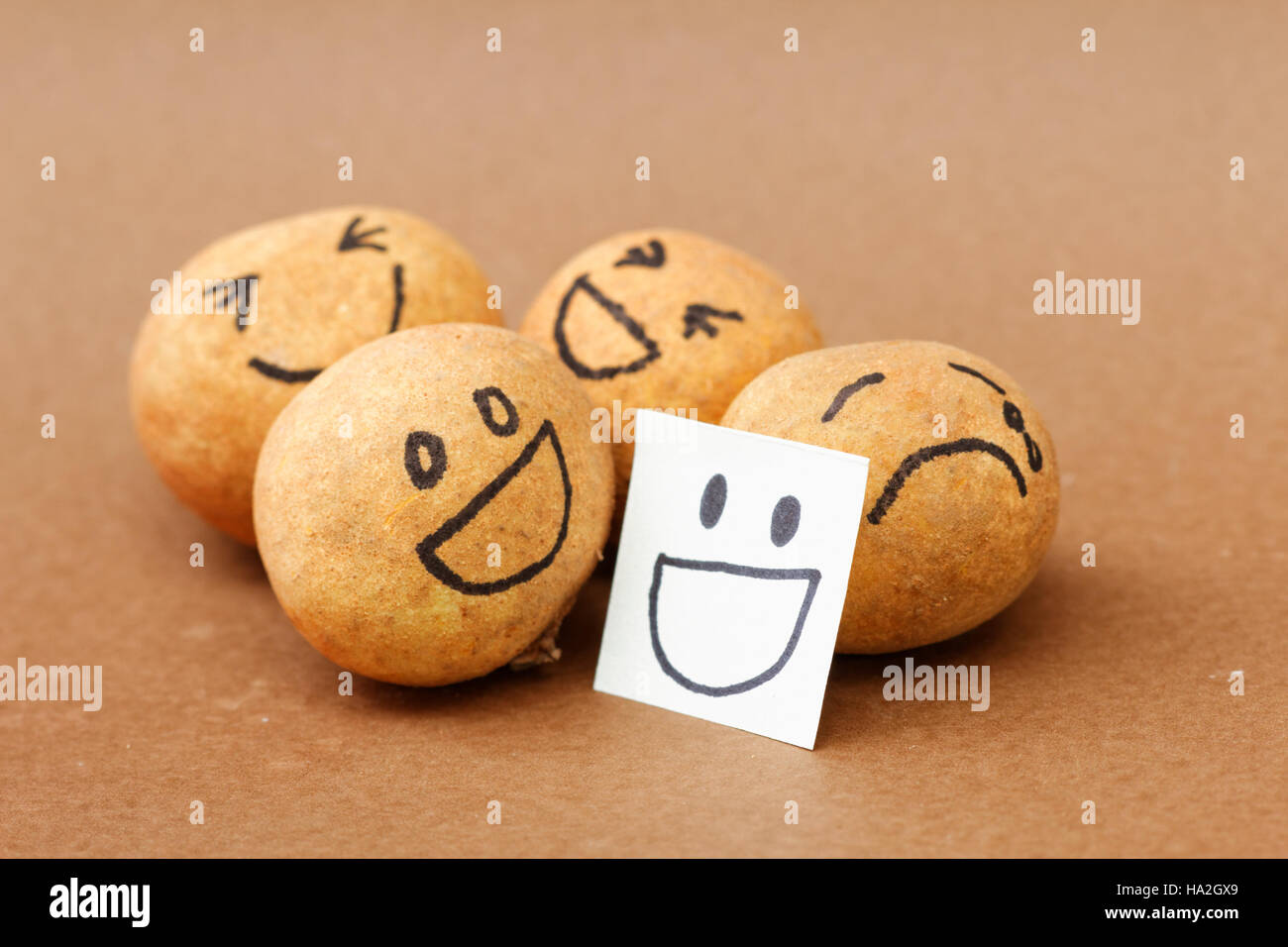 Un gruppo di sfera marrone a ridere con uno della sfera piangendo dietro una maschera sorridente concettuale. Foto Stock