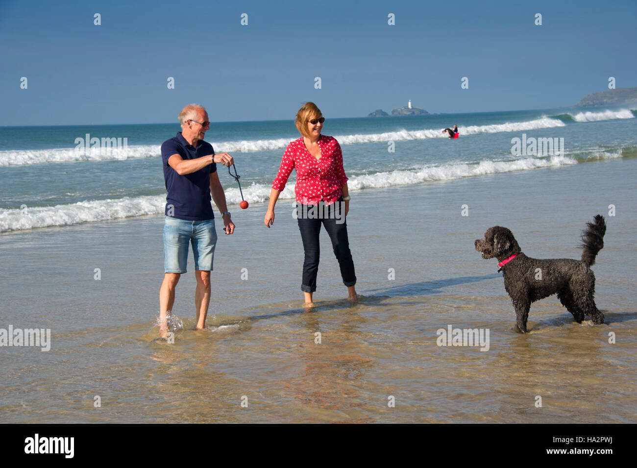 Una coppia matura (maschio e femmina) indossando vestiti estivi con il loro cane divertirsi su una soleggiata spiaggia della Cornovaglia. Foto Stock