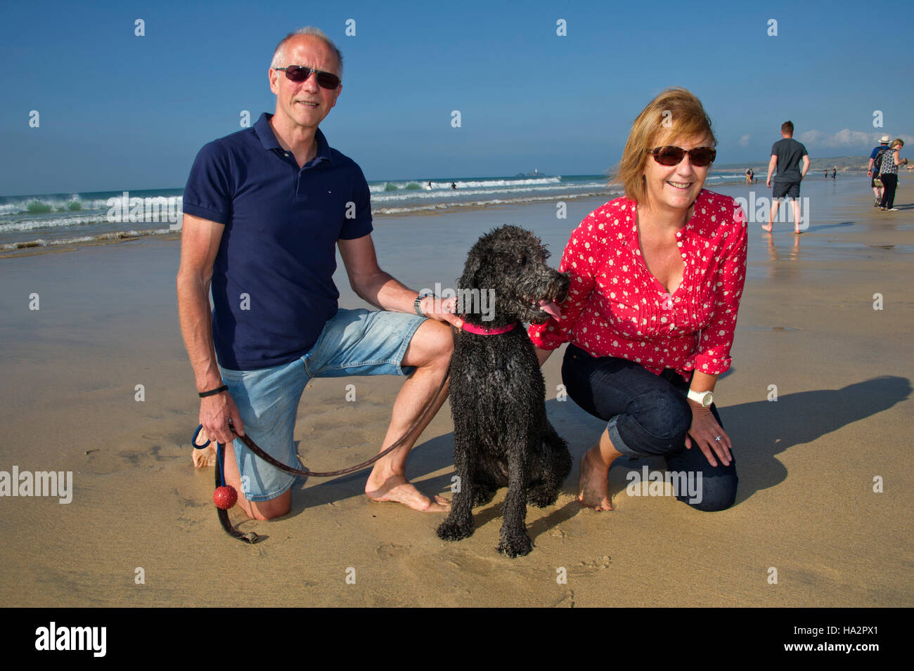 Una coppia matura (maschio e femmina) indossando vestiti estivi con il loro cane divertirsi su una soleggiata spiaggia della Cornovaglia. Foto Stock