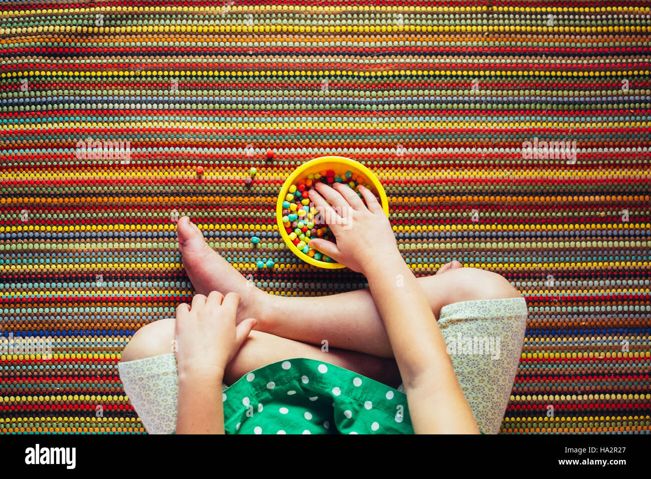 Ragazza seduta a gambe incrociate mangiare snack multicolore Foto Stock