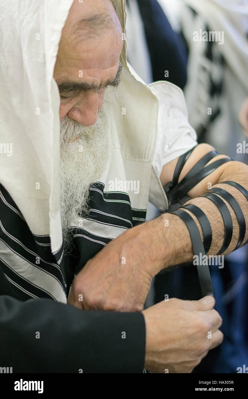 Un vecchio uomo ebraico con la barba mettendo sul tefillin in una sinagoga a Montefiore cimitero di Cambria Heights, Queens, a New York. Foto Stock