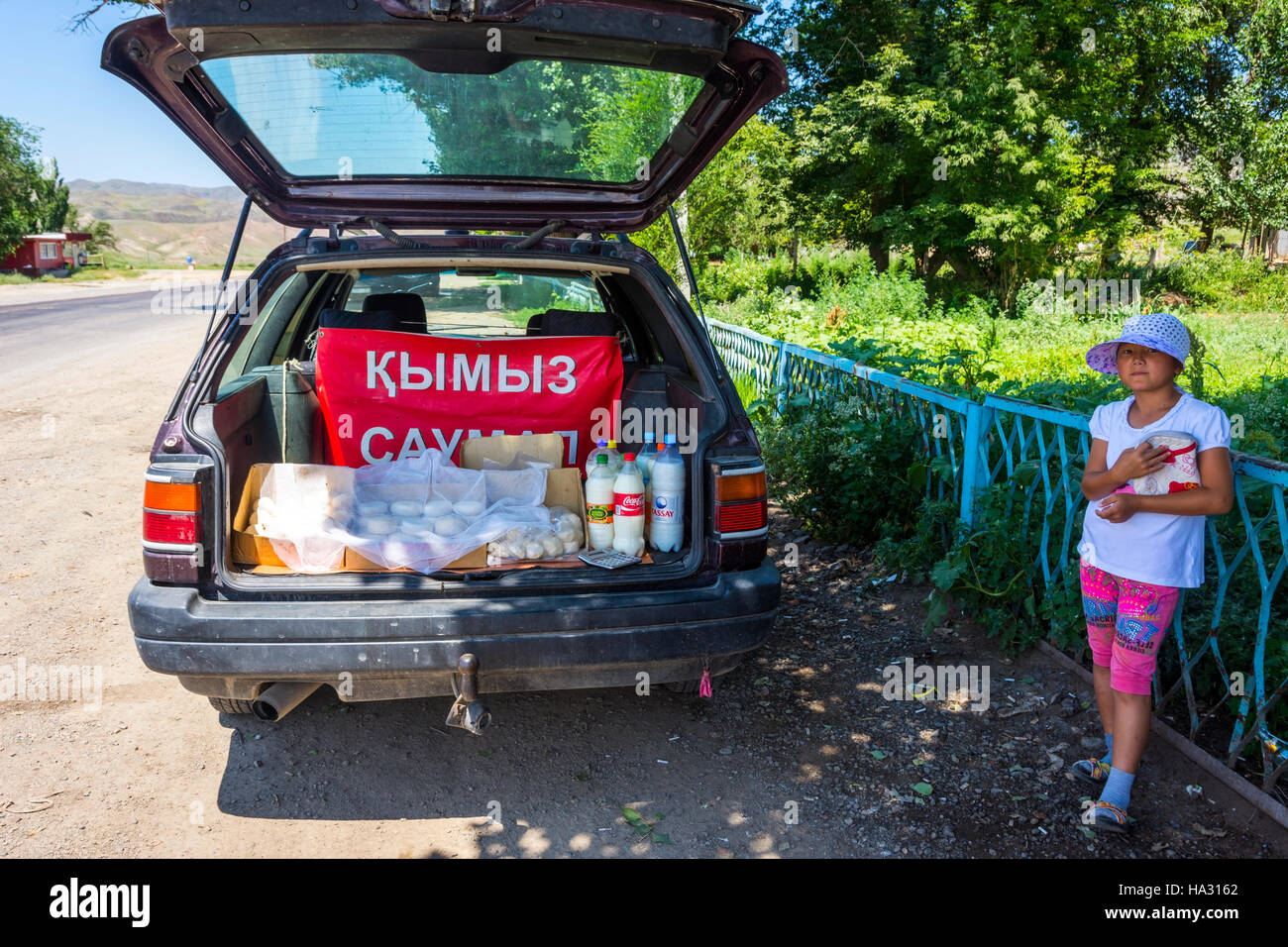 ALMATY, KAZAKHSTAN - 10 Luglio: Ragazza la vendita di formaggio e kumis, il kazako popolare bevanda fatta della fermentazione del latte di cavallo dalla vettura in strada. Luglio 2016 Foto Stock