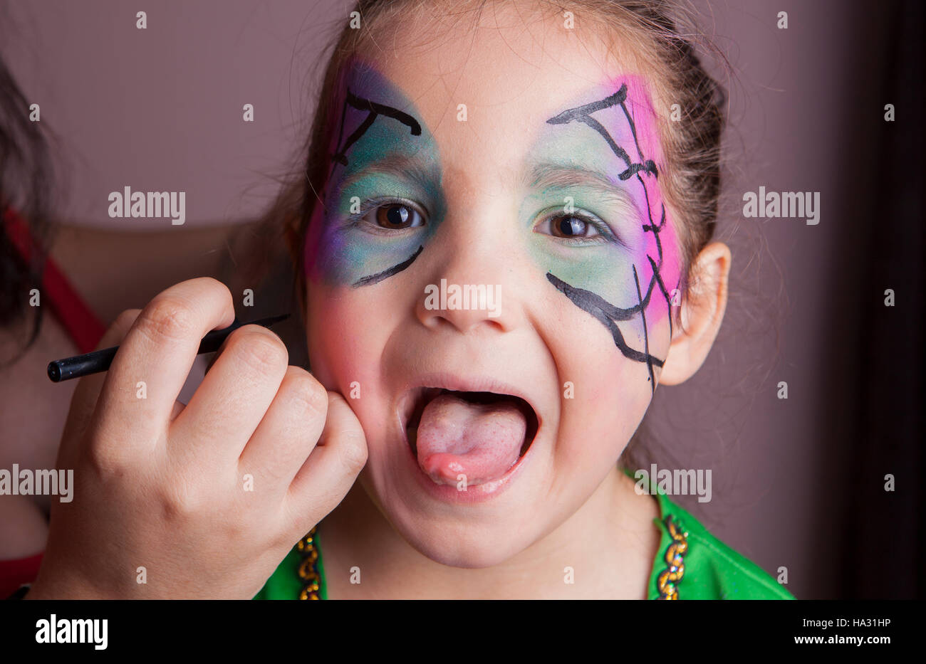 Bambina con la lingua di fuori mentre essa è composta da make-up artist Foto Stock