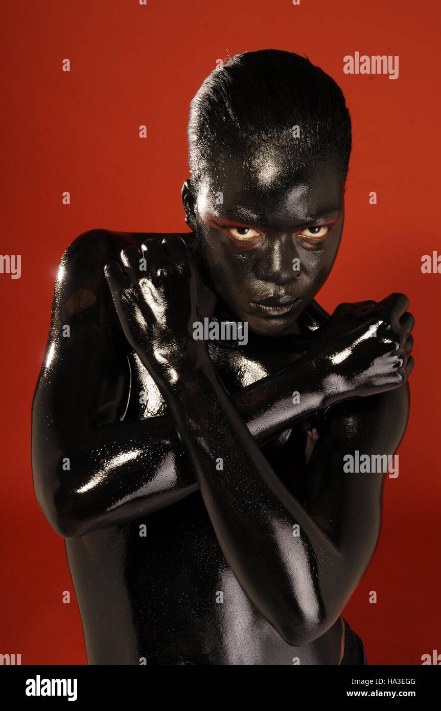 Una femmina nero modello bodypainted in nero contro uno sfondo di colore rosso. Foto Stock