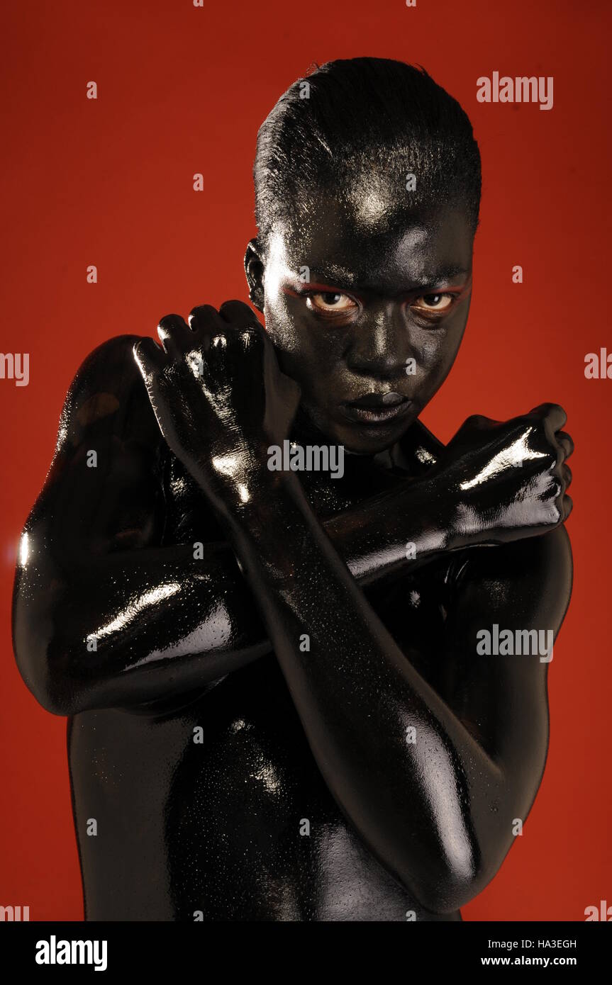 Una femmina nero modello bodypainted in nero contro uno sfondo di colore rosso. Foto Stock