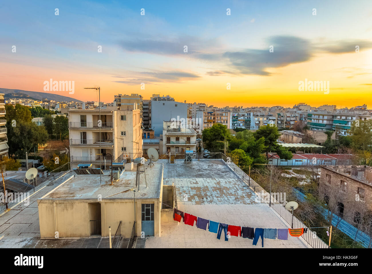 Servizio lavanderia appesi a corde sulla cima di un blocco di negozi contro un paesaggio urbano e il tramonto in Grecia Foto Stock