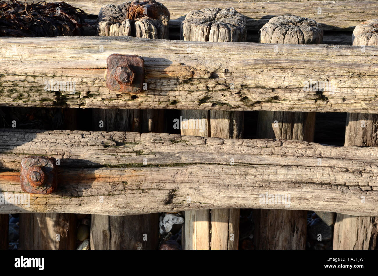Resti di struttura in legno una volta costruito per la protezione delle coste, ora lasciato al suo destino. Robusto legno e viti arrugginite. Foto Stock