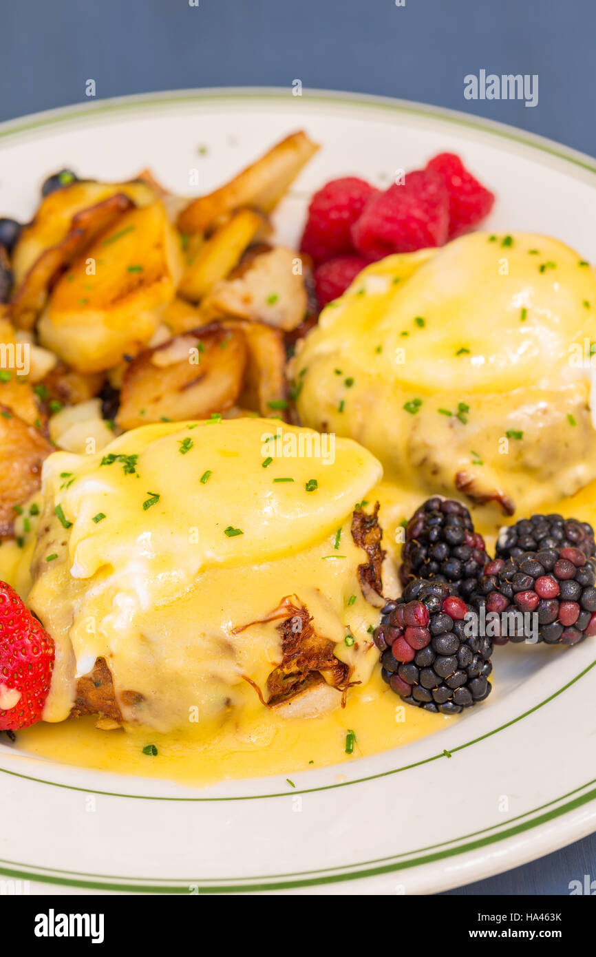 Crabcake uova Benedict servita con frutti di bosco e patate tedesche Foto Stock