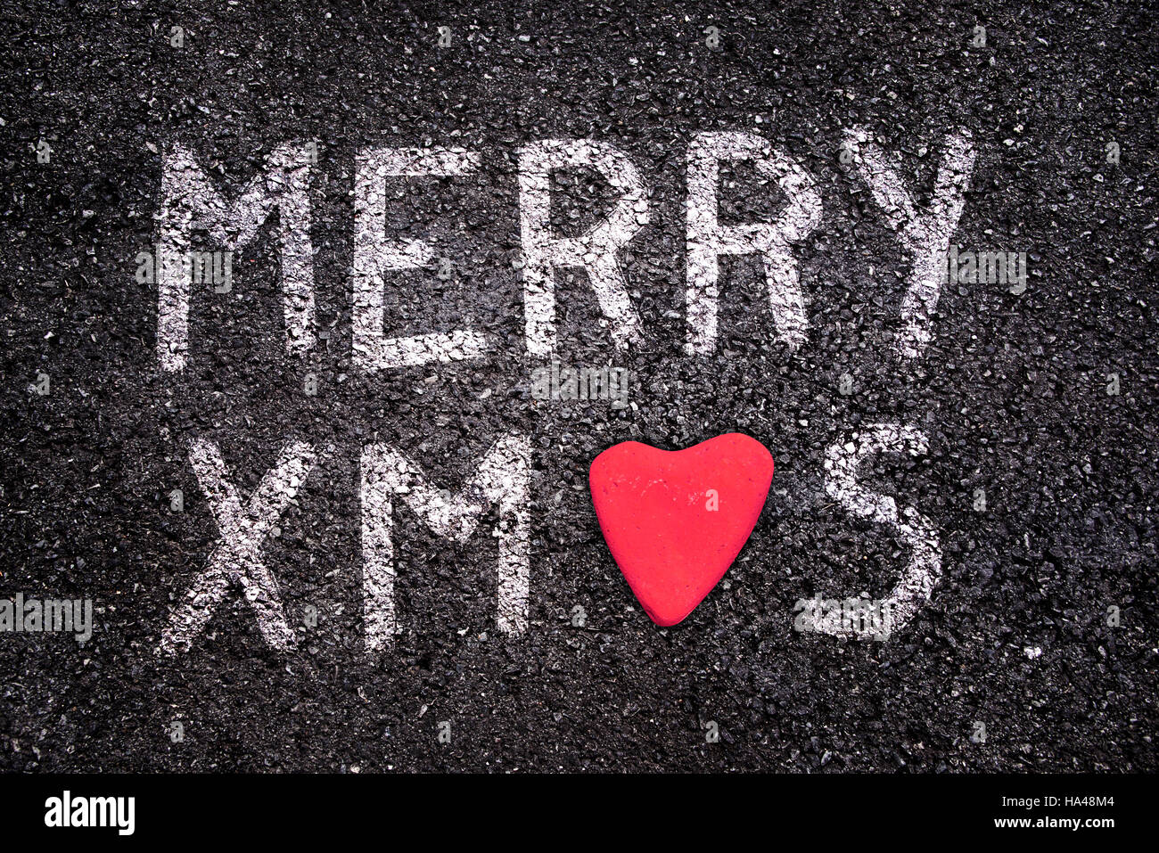 Merry Xmas scritto su strada asfaltata, pietra rossa a forma di cuore Foto Stock