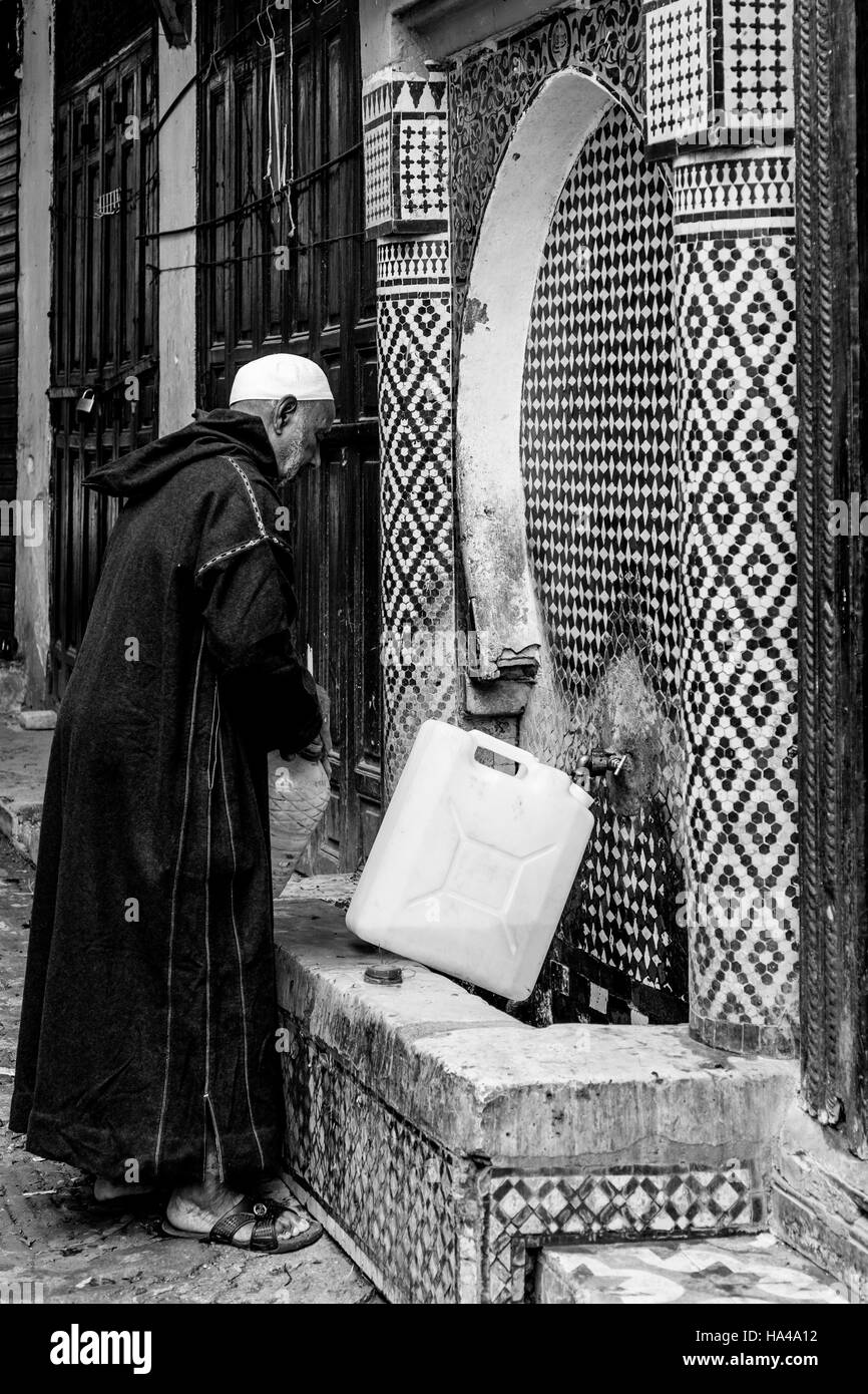 Un anziano uomo raccoglie acqua da un pubblico fontana di acqua nella Medina di Fez el Bali, Fez, in Marocco Foto Stock
