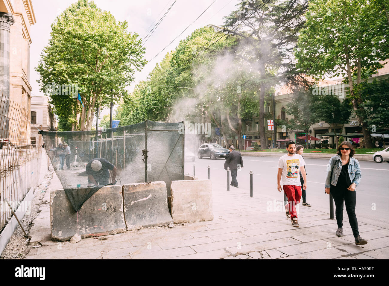 Tbilisi, Georgia - 20 Maggio 2016: i passanti la gente camminare lungo la zona di riparazione della pavimentazione sulla Rustaveli Avenue nella giornata di primavera. Foto Stock