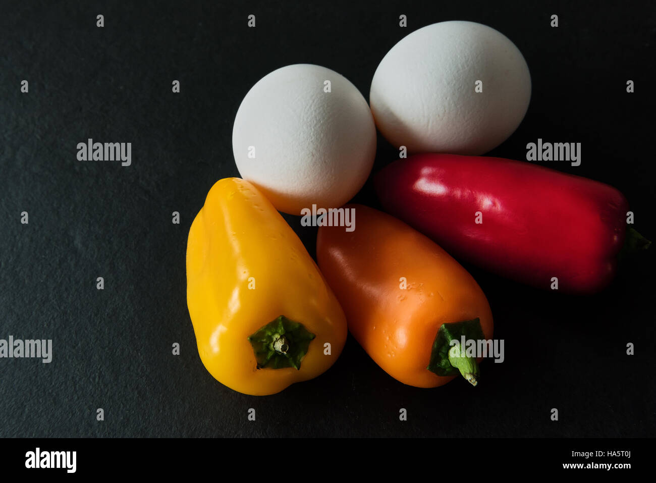 Low Carb - due uova di colore bianco con tre mini colorati paprikas al buio su un sfondo di ardesia Foto Stock