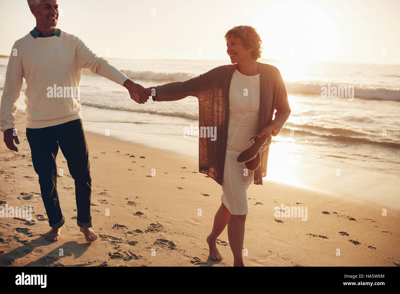 Colpo all'aperto di romantica coppia senior camminando lungo la riva del mare tenendo le mani. Senior l uomo e la donna di camminare sulla spiaggia insieme al tramonto. Foto Stock