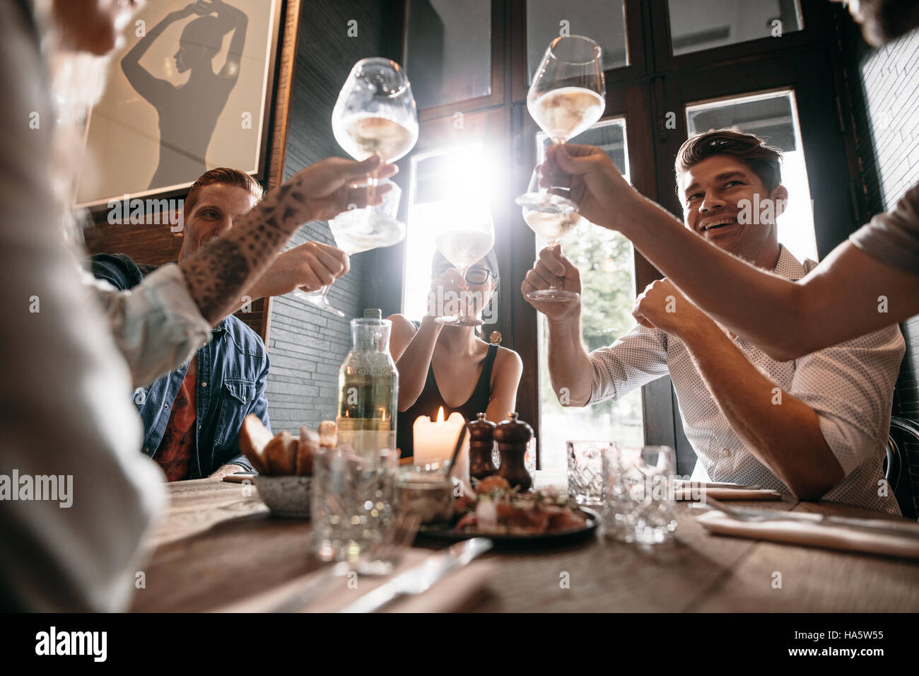 Gruppo di giovani di fare un brindisi al ristorante. Gli uomini e le donne sedute a un tavolo in cafe e tostatura del vino. Foto Stock