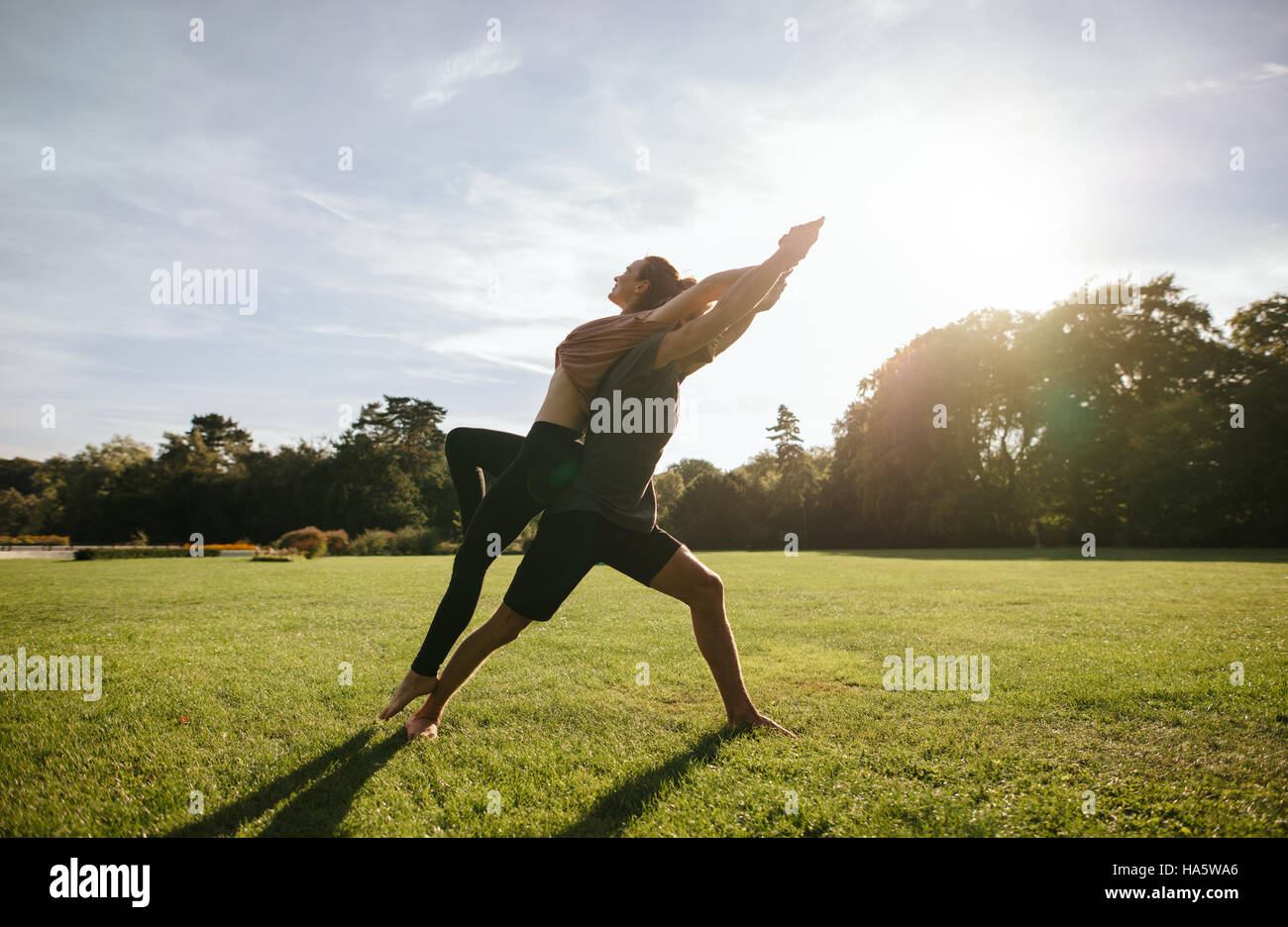 Colpo all'aperto del giovane uomo e donna fare yoga in coppia. Giovane facendo acrobatici esercizi di yoga al parco. Foto Stock