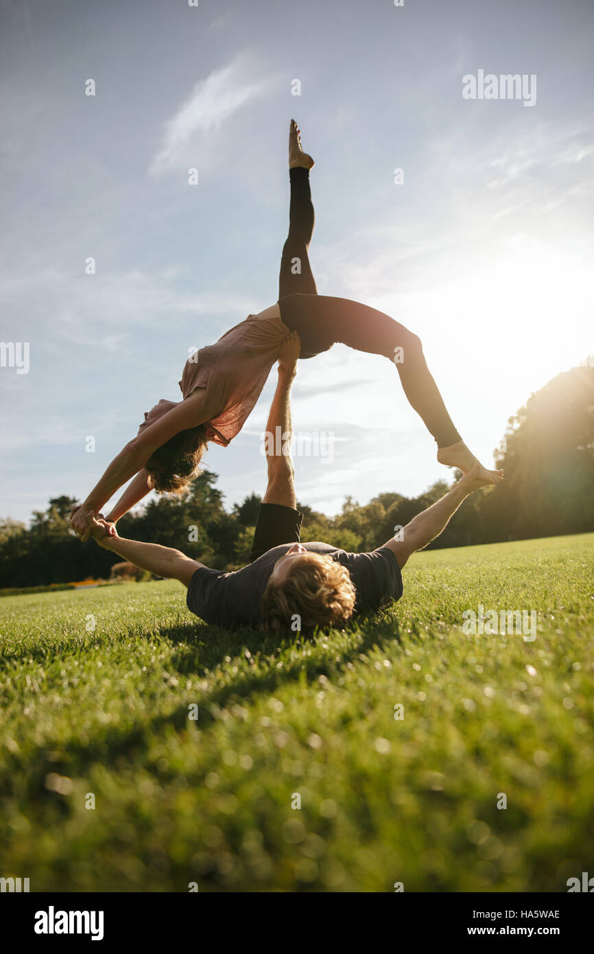 Colpo verticale di una sana coppia giovane facendo acro yoga sull'erba. L uomo e la donna che esercitano in coppia al parco. Foto Stock