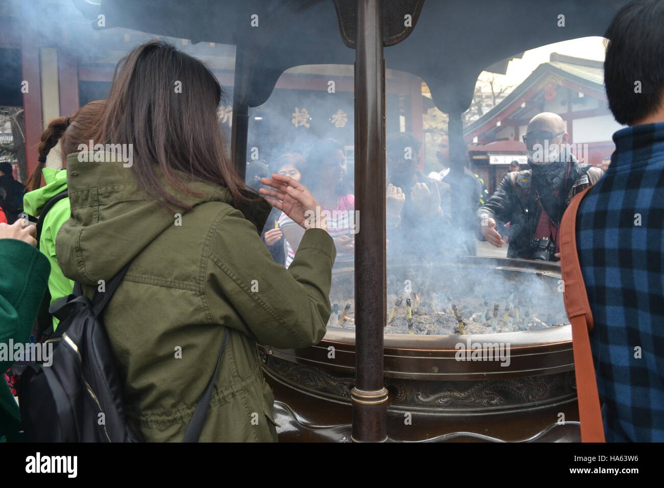 Tokyo, Japan-2/28/16: Donna in verde (insieme ad altri) si riunisce intorno allo jokoro del Tempio Sensoji di Asakusa per far ondeggiare il fumo dell'incenso. Foto Stock