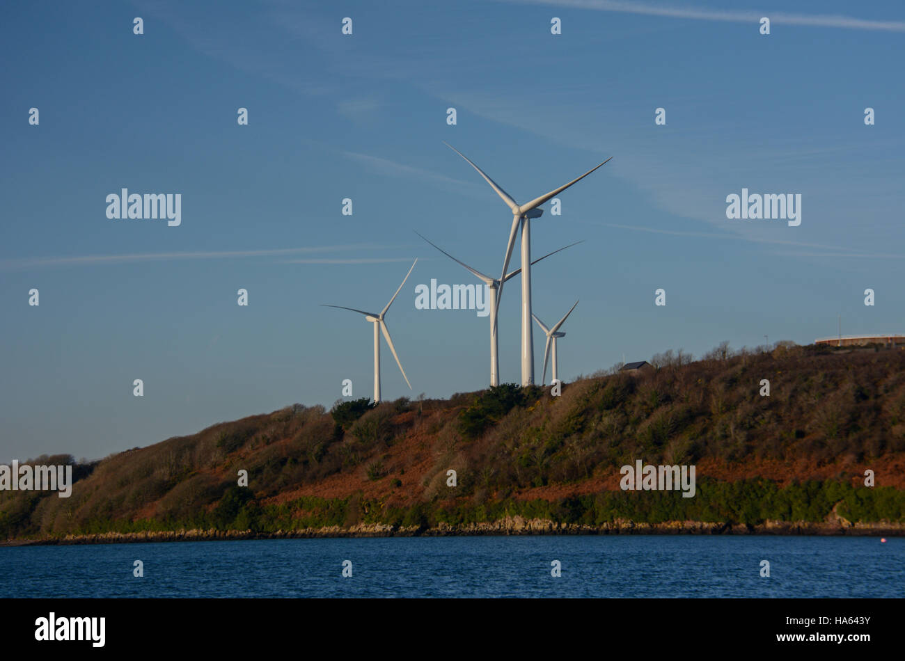 Le turbine eoliche contro un cielo blu con ciuffi di cirrus nuvole. Litorale di verde e marrone di vegetazione con calma il mare blu profondo Foto Stock
