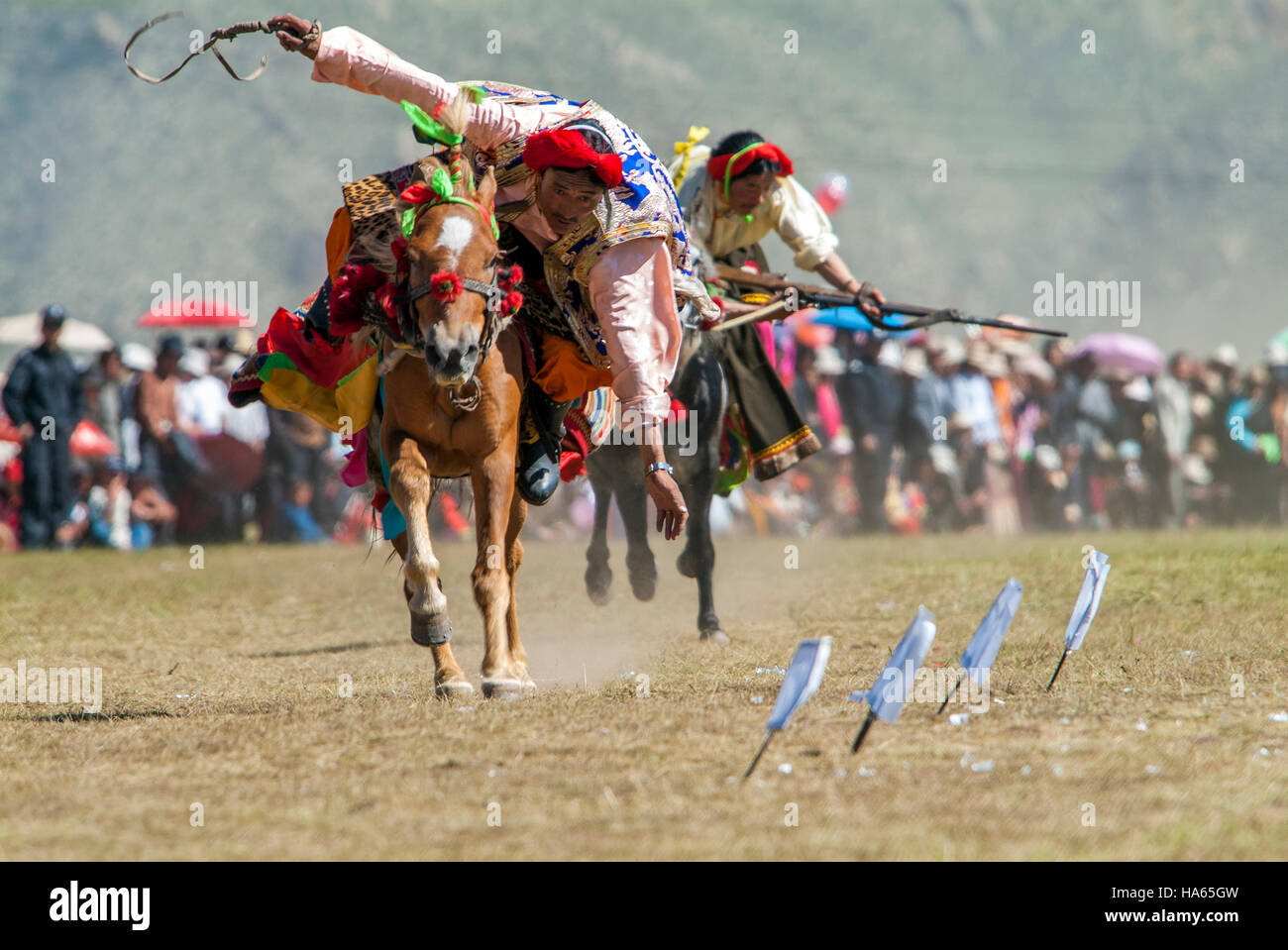 Khampa horseman sparare pezzi di carta con pietra focaia pistole di bloccaggio dal dorso di un cavallo al galoppo a Yushu Horse Racing Festival. Qinghai, Cina. Foto Stock