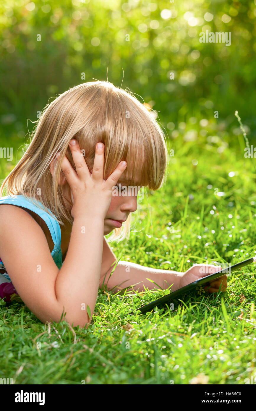 Bambina con un touch pad in un giardino estivo Foto Stock