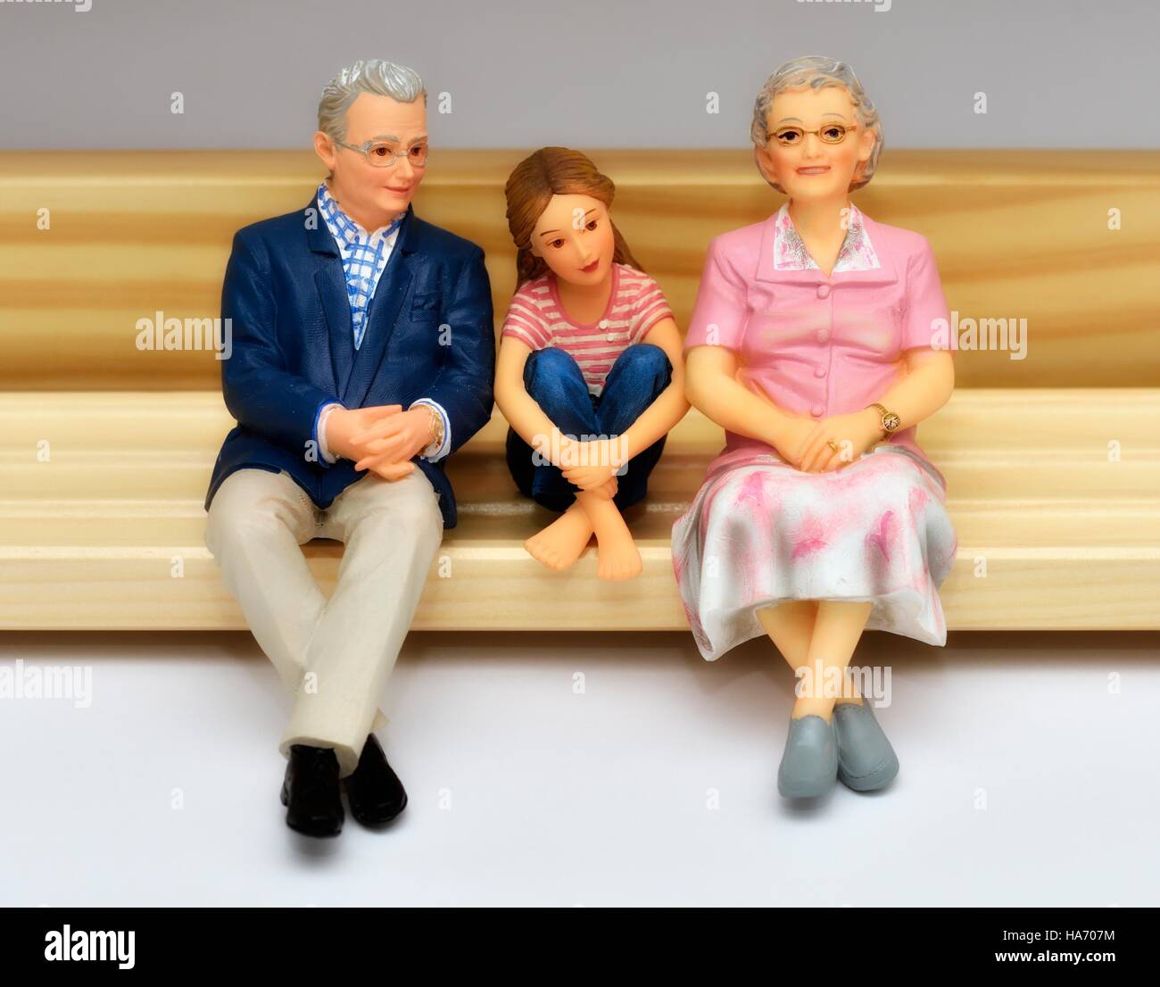Un anziano senior statuetta in miniatura giovane seduta su una panchina con il loro nipote Foto Stock