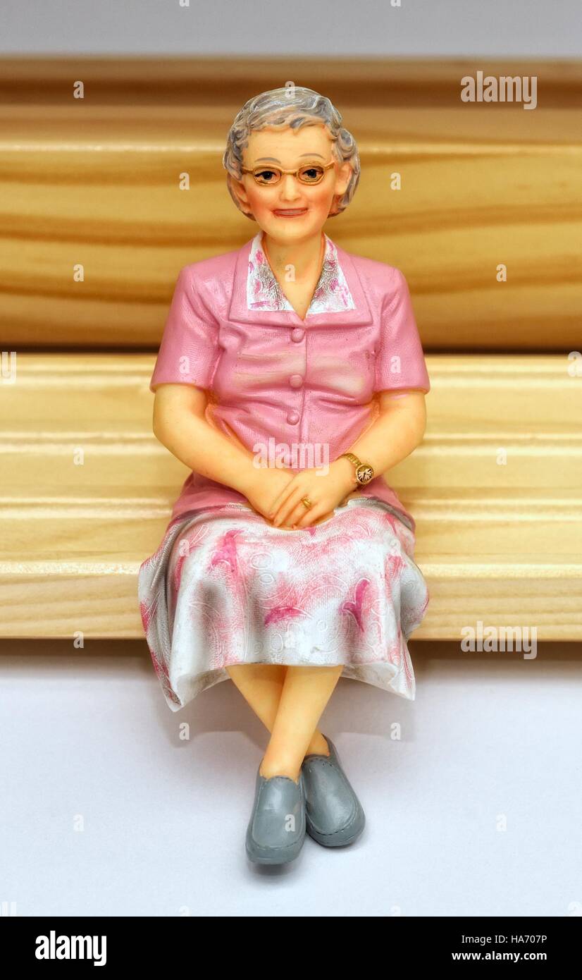 Una donna anziana pensionata senior statuetta in miniatura seduta su una panca in legno. Foto Stock
