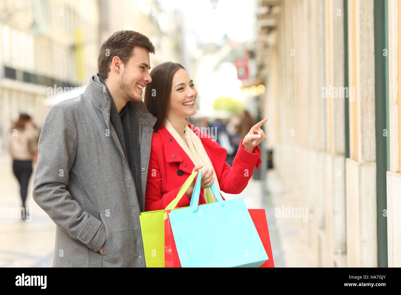 Paio di consumatori a guardare vetrine e tenendo le borse della spesa in strada in inverno Foto Stock