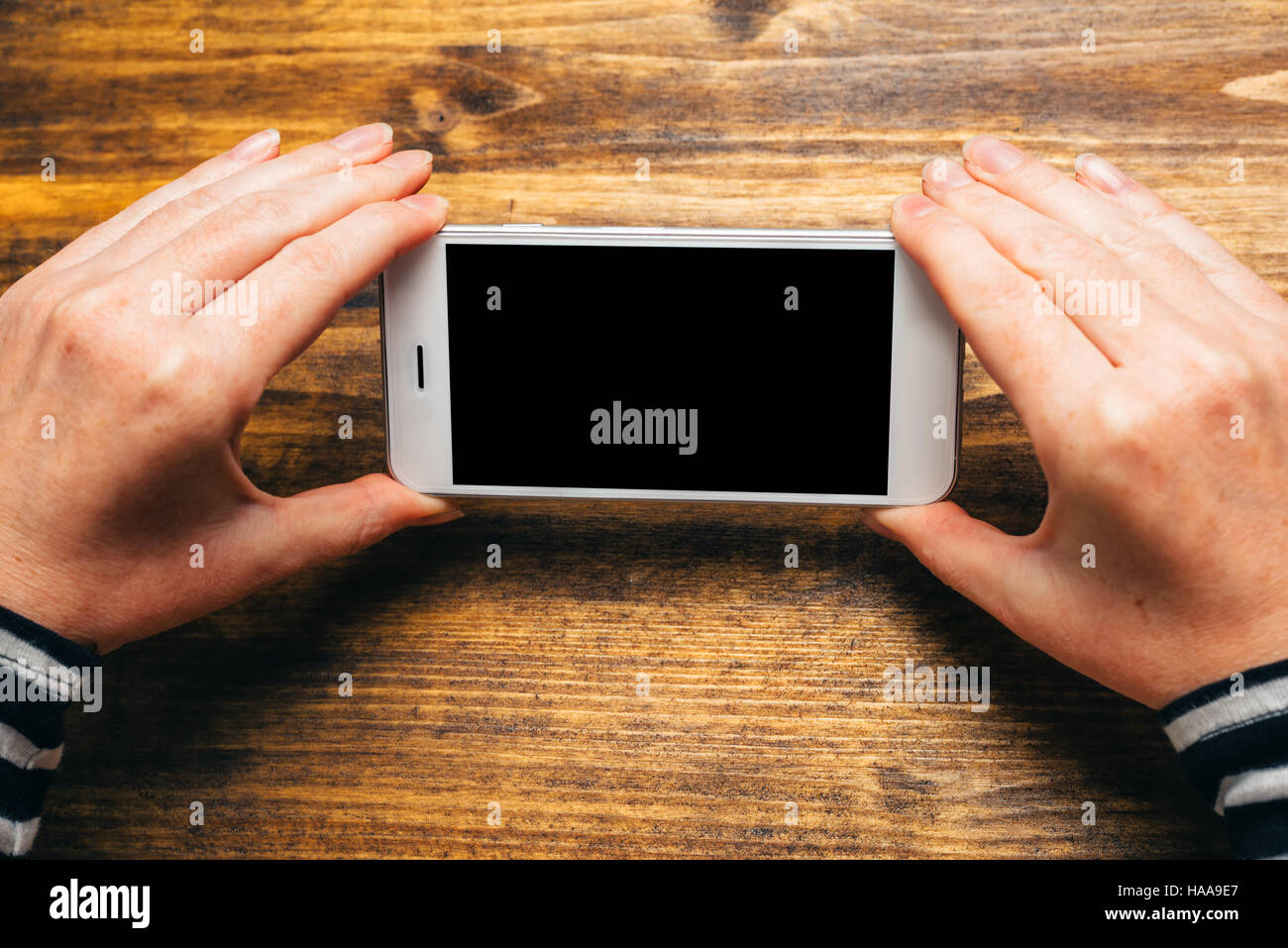Donna che utilizza smart phone in orizzontale con orientamento orizzontale per lo streaming di filmati o sfogliare foto gallery, schermo vuoto come spazio di copia Foto Stock