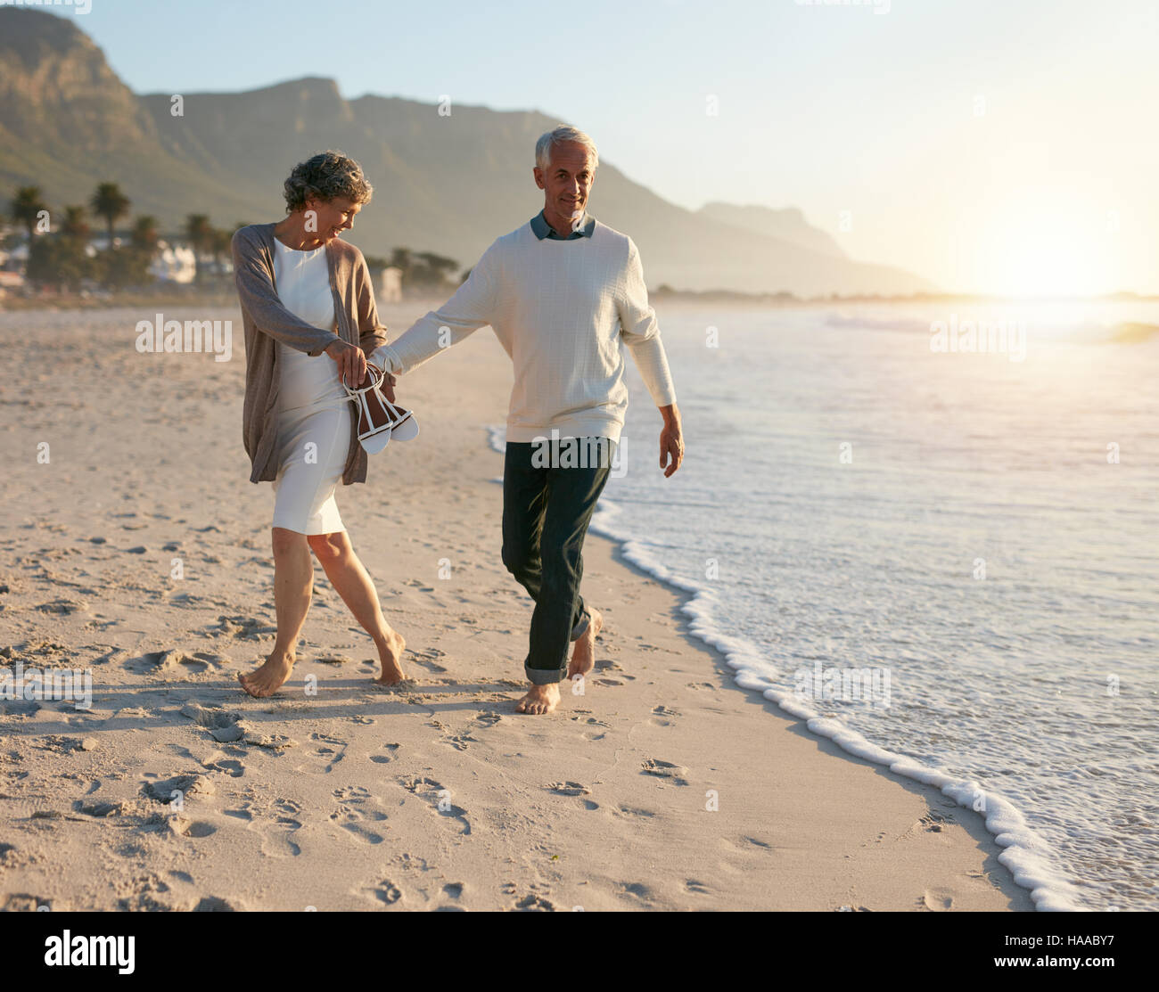 Coppia senior comodamente a piedi sulla spiaggia tenendo le mani. Godersi la vacanza estiva sulla spiaggia. Foto Stock