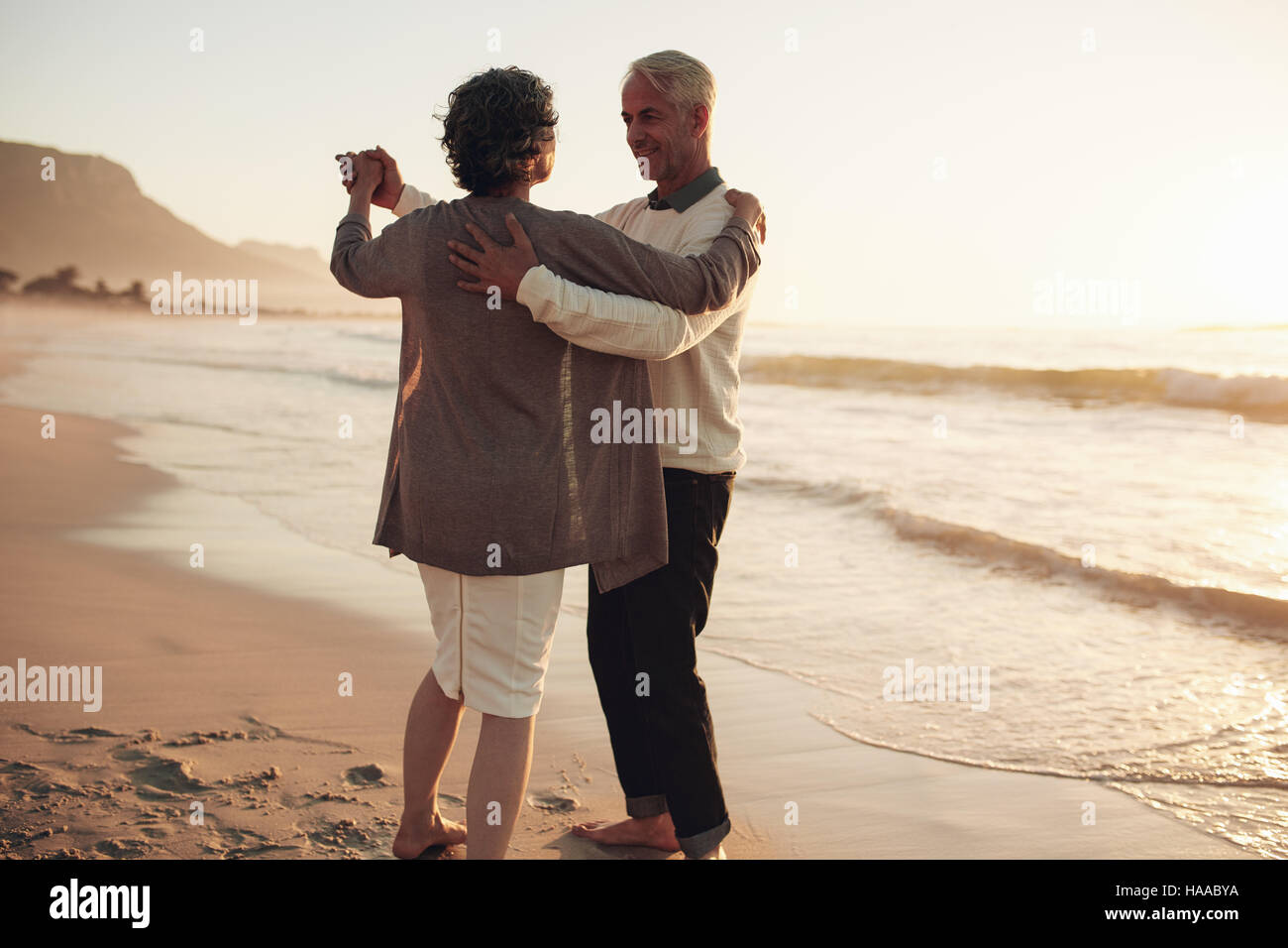 Senior l uomo e la donna coppia danzante al tramonto sulla riva del mare. Coppia matura godendo una romantica giornata in spiaggia. Foto Stock