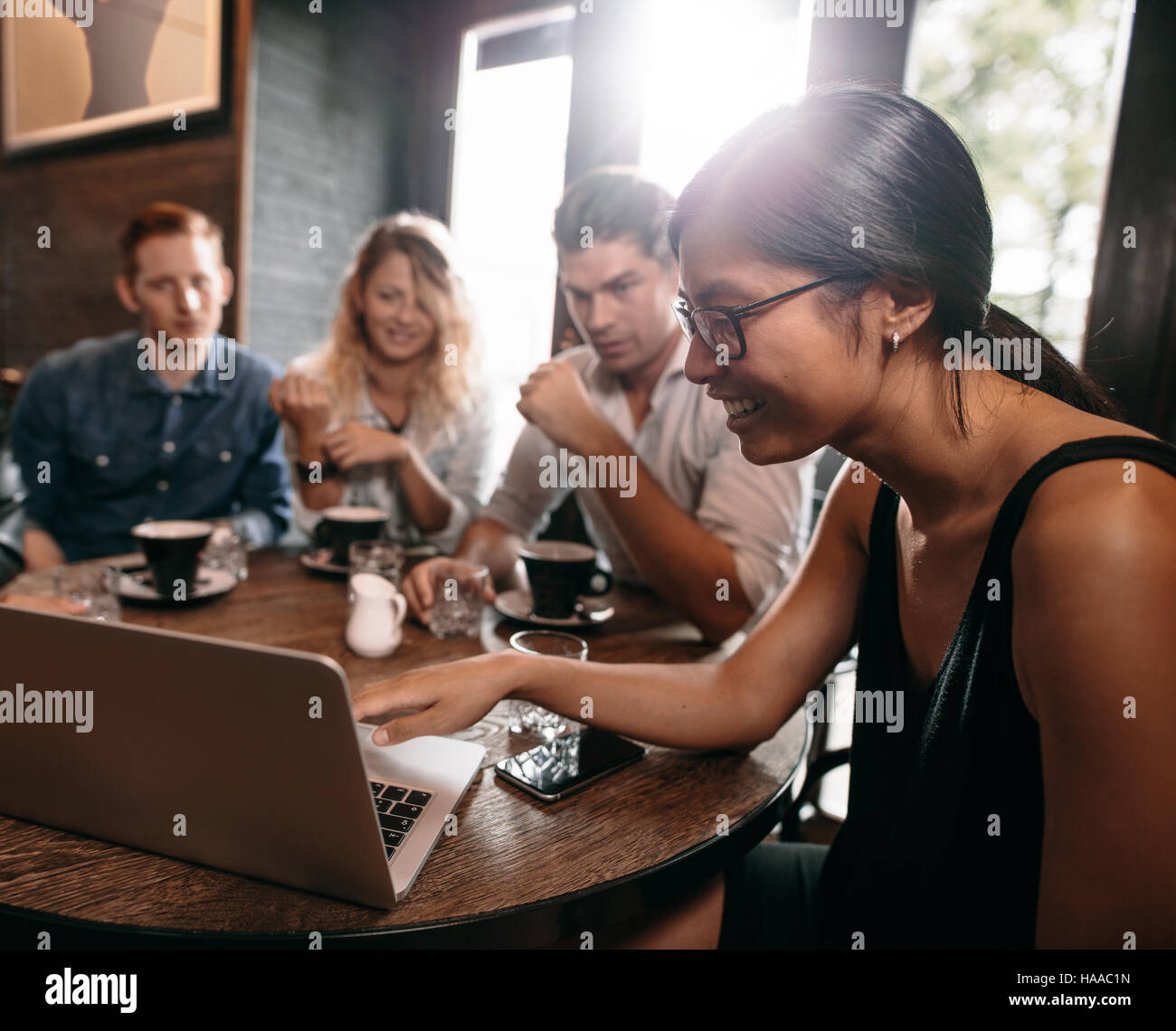 Gruppo di amici in cafe guardare qualcosa online su laptop. Giovani uomini e donne al ristorante guardando il laptop. Foto Stock