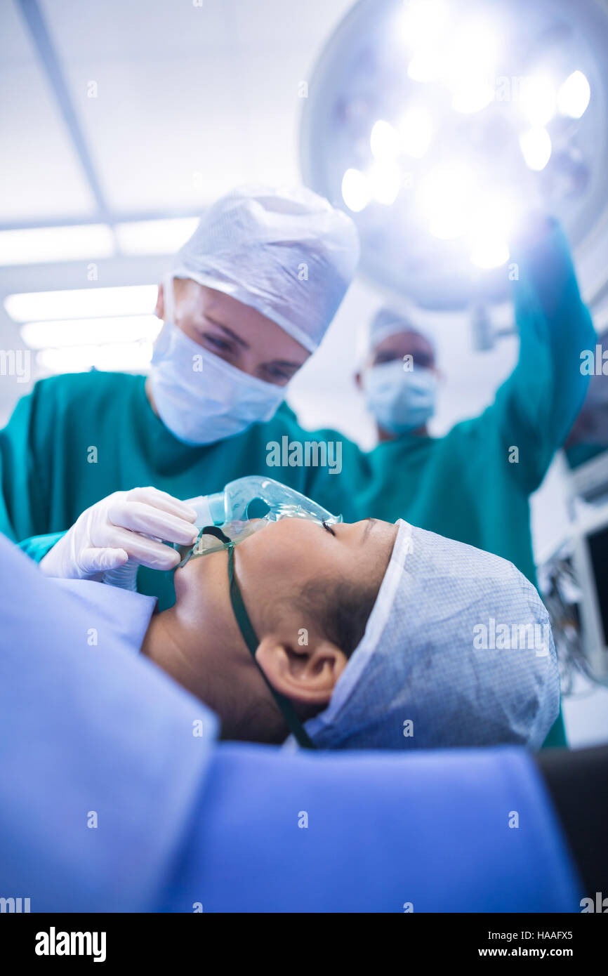 Chirurgo regolando le maschere di ossigeno sulla bocca del paziente nel teatro di funzionamento Foto Stock