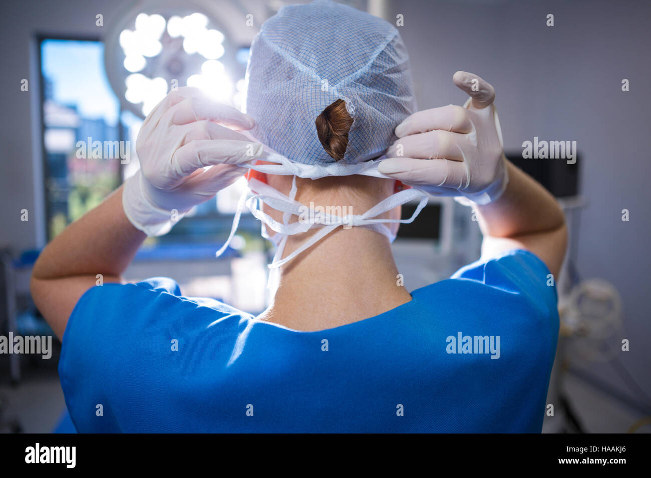 Vista posteriore di infermiera femmina indossa cappuccio chirurgico nel teatro di funzionamento Foto Stock