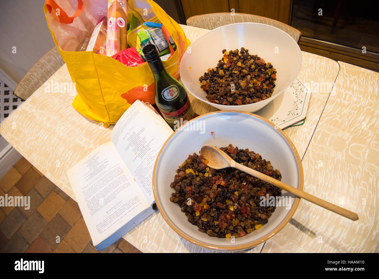 Cucina tradizionale recipiente di miscelazione pieno di frutta imbevuto di acquavite con un apri libro di cucina e la ricetta per la ricca torta di Natale con ingredienti in un Foto Stock