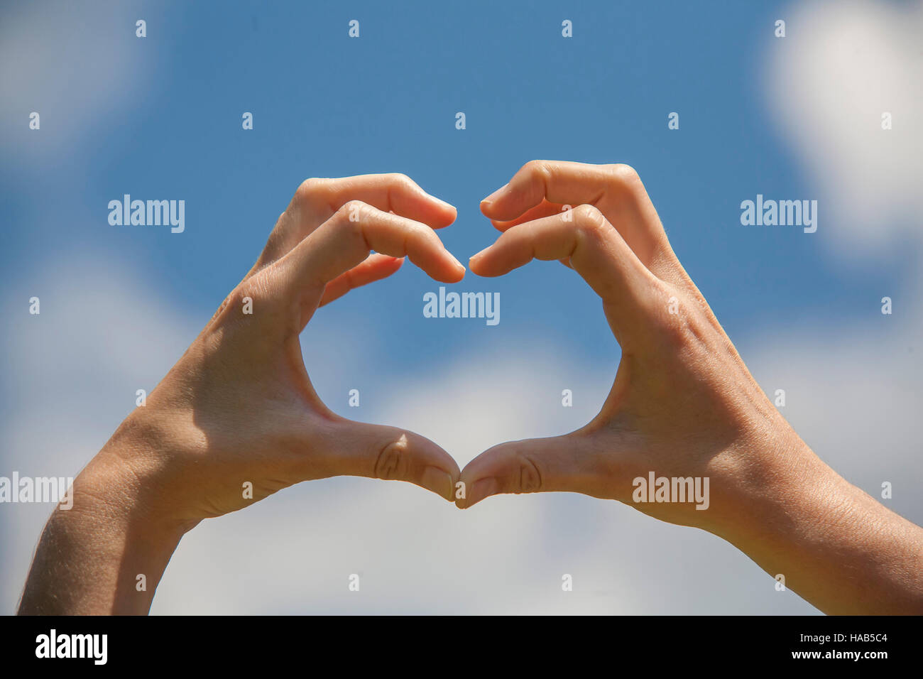 Simbolo di amore, di mani umane in forma di cuore verso il cielo blu Foto Stock