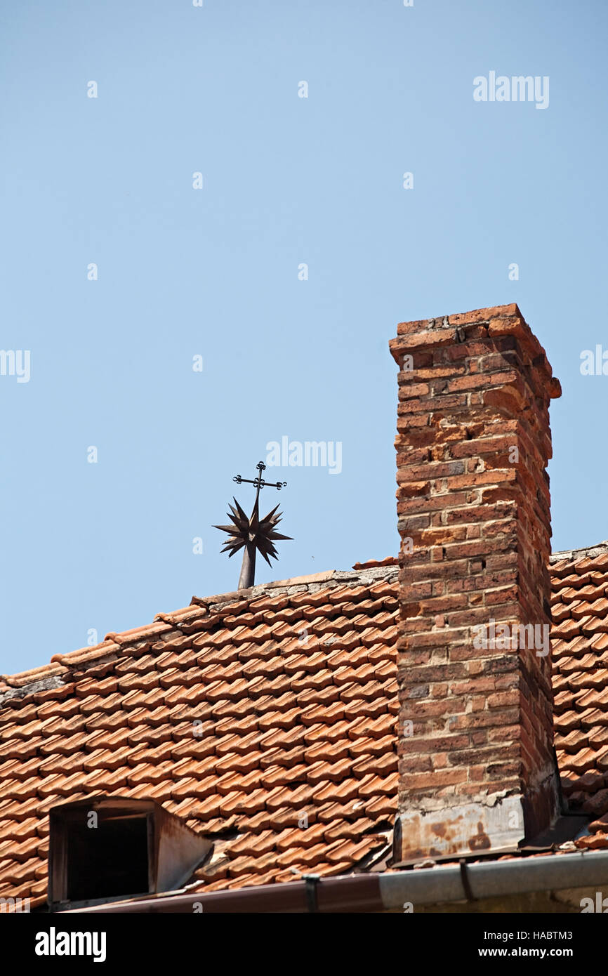 Rosso tetto di tegole con camino in mattoni e paletta metallica closeup sul cielo blu sullo sfondo Foto Stock