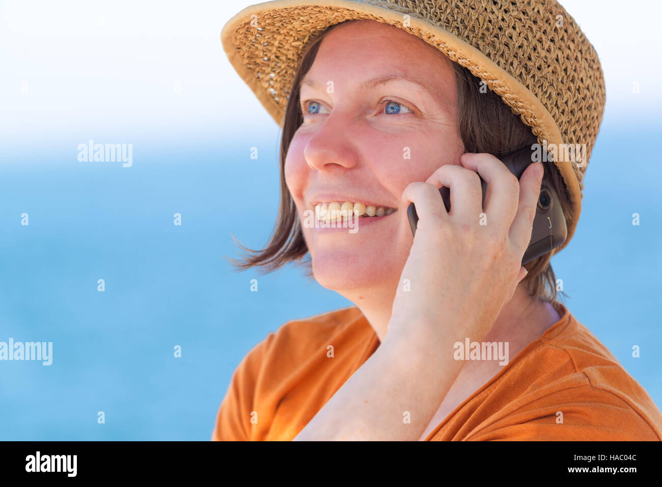 Bella adulto donna caucasica indossando Elegante cappello di paglia è utilizzando il telefono cellulare su Vacanze Estate Mare Vacanze Foto Stock