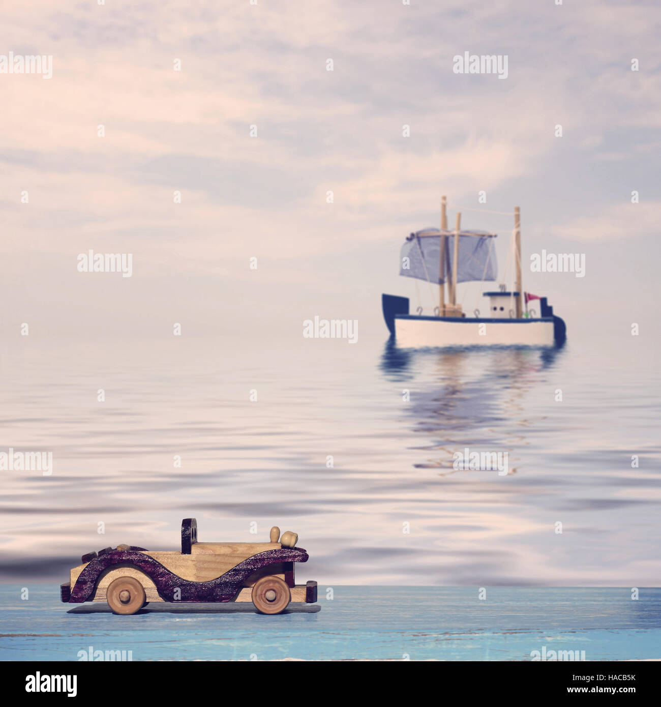 Giocattolo auto su un blu superficie di legno e il giocattolo in barca a vela in mare Foto Stock