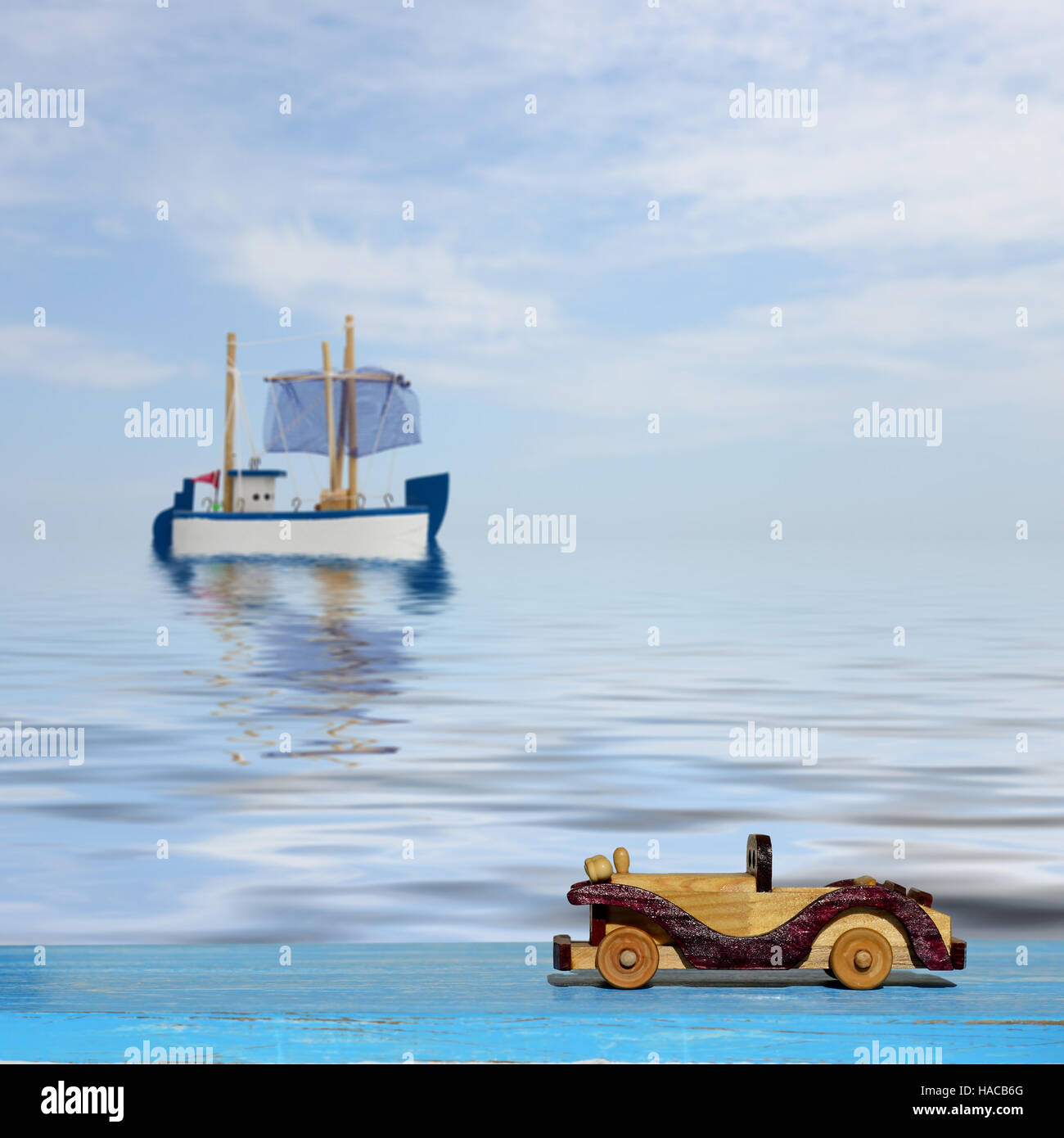 Giocattolo auto su un blu superficie di legno e il giocattolo in barca a vela in mare Foto Stock