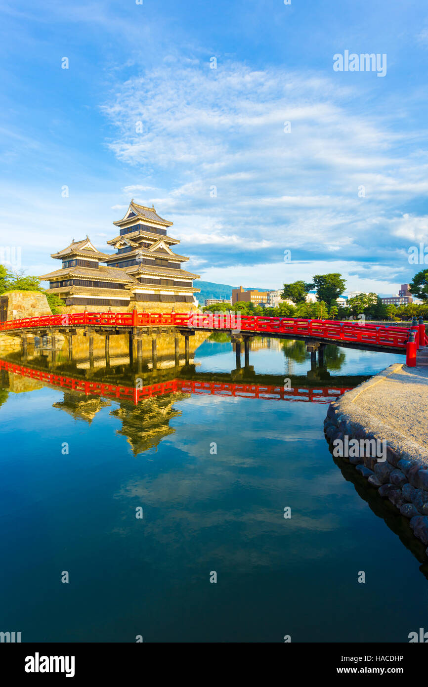 Fossato acquosa mostra riflessi di colore rosso brillante tradizionale ponte di legno, cielo nuvoloso e l'antico mastio del castello Matsumoto Foto Stock