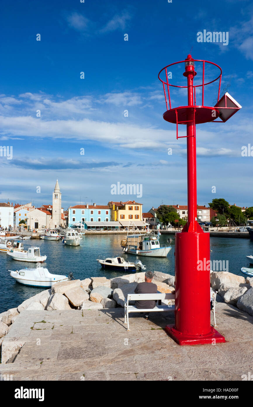 Uomo seduto su un banco di lavoro accanto al faro rosso con pannello solare nel porto di Fazana in Croazia Foto Stock