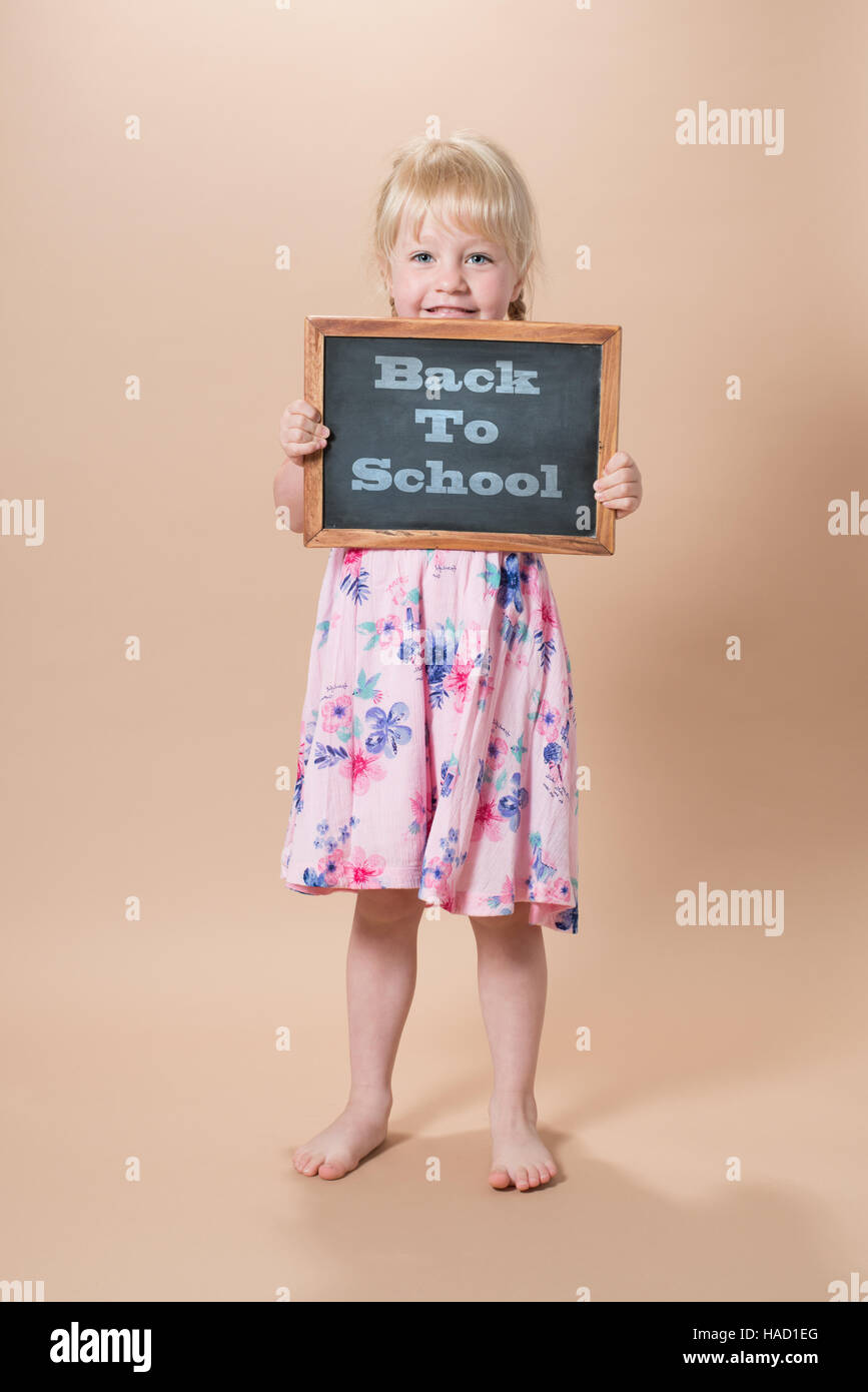 Bambina in età scolare tenendo chalk board con "Si torna a scuola" messaggio Foto Stock